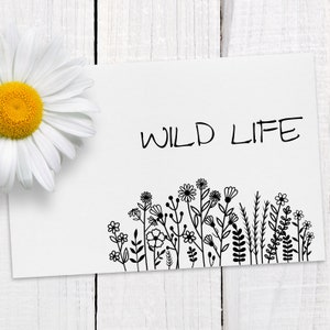 Op de afbeelding: Een witte kaart met de tekst "WILD LIFE" in zwarte letters. Onderaan de kaart staat een zwart-witte illustratie van een rij wilde bloemen.