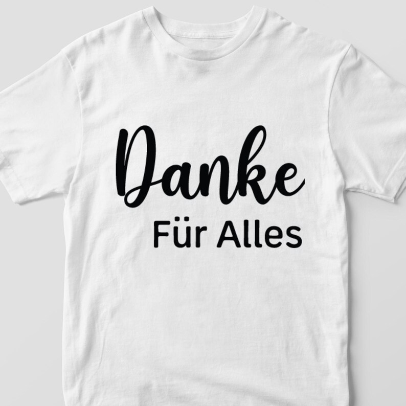 May include: White t-shirt with the German text "Danke F&uuml;r Alles" in black script. The shirt has a crew neck and short sleeves. The text translates to "Thanks for everything."