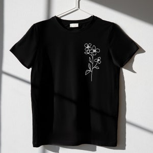 May include: A black t-shirt with a white line drawing of a flower on the left side of the chest.