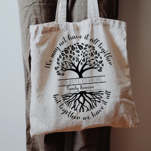 May include: A white canvas tote bag with a black tree design and the text "We may not have it all together but together we have it all". The text is in a cursive font. There is a blank space for text that says "YOUR TEXT HERE" and "Family Reunion".