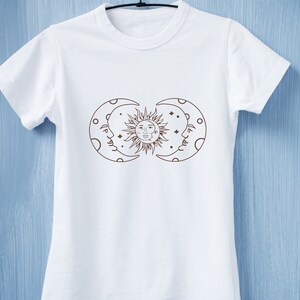 May include: White t-shirt with a brown line drawing of a sun and two moons with faces.