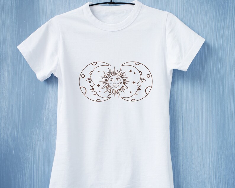 May include: White t-shirt with a brown line drawing of a sun and two moons with faces.