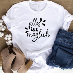 Peut inclure: T-shirt blanc avec un texte noir qui dit "alles ist moglich", ce qui se traduit par "tout est possible".