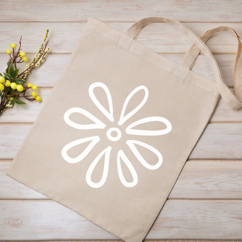 May include: A beige tote bag with a white daisy design. The bag has a long handle that can be worn over the shoulder.