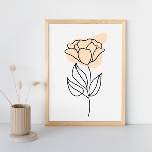 May include: A framed print of a minimalist line drawing of a flower with a peach-coloured background. The flower is drawn in black and has a single stem with leaves.