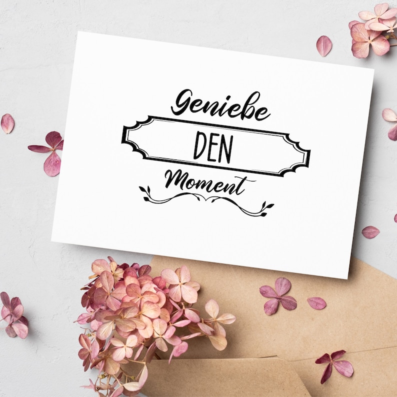 Peut inclure: Carte blanche avec du texte noir qui dit "Genie&szlig;e den Moment" dans une police d&eacute;corative. La carte est entour&eacute;e de fleurs roses.