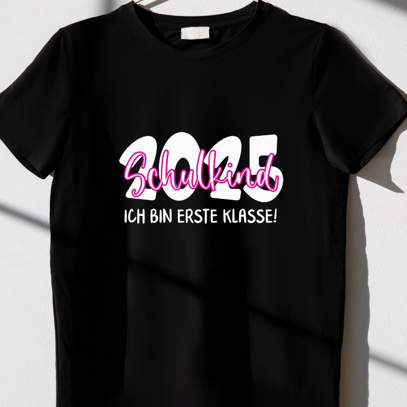 Pode incluir: Camiseta preta com texto branco que diz "2025 Schulkind Ich bin erste Klasse!"