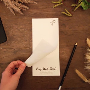 Könnte beinhalten: Eine weiße Karte mit dem Text "Pray. Wait. Trust." und der Schrift "Hört nicht auf zu Beten. (1. Thessalonicher 5:17)" darauf gedruckt. Die Karte hat oben ein kleines Kreuz mit einem Rankenmuster.