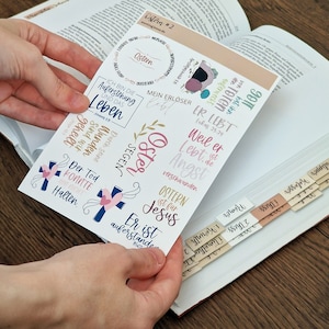 Könnte beinhalten: Ein Blatt mit bunten Aufklebern mit christlichen Osterbotschaften. Die Aufkleber zeigen Sätze wie "Ostern", "Mein Erlöser", "Er Lebt", "Weil er Lebt, ist die Angst verschwunden", "Ostern ist für Jesus", "Er ist auferstanden", "Der Tod konnte ihn nicht halten", "Segen", "Wunder", "Durch seine Wunden sind wir geheilt".