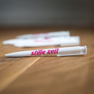 Könnte beinhalten: Weißer Stift mit einer pinkfarbenen Aufschrift "stille zeit" auf einer Holzoberfläche.