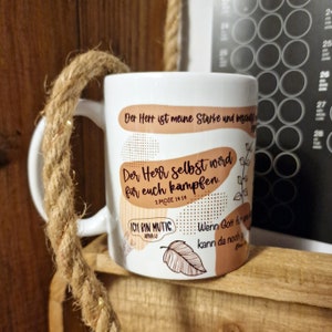 Könnte beinhalten: Weiße Keramiktasse mit braunem Henkel. Die Tasse hat ein braunes und weißes Design mit dem Text "Der Herr ist meine Starke und beschützt mich" und "Der Herr selbst wird für euch kämpfen. 2 Mose 14:14". Es gibt auch ein braunes Blatt mit dem Text "Ich bin mutig.  Nehemia 4:13" und dem Text "Wenn Gott für uns ist, kann da noch jemand gegen uns sein?"