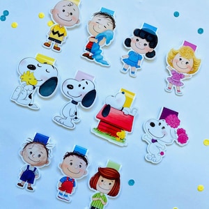 Puede incluir: Un conjunto de 12 imanes de marcapáginas coloridos con personajes de la tira cómica Peanuts. Los imanes presentan personajes como Charlie Brown, Snoopy, Lucy y Linus.