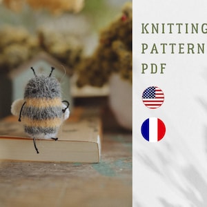 Könnte beinhalten: Eine handgestrickte Bienenfigur mit grauen, gelben und weißen Streifen, schwarzen Fühlern und kleinen Flügeln. Das Bild enthält den Text "KNITTING PATTERN PDF" und die amerikanische und französische Flagge.