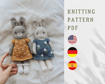 May include: Knitting pattern PDF for two grey bunny dolls wearing dresses. The bunny on the left is wearing a yellow dress with white hearts. The bunny on the right is wearing a blue dress with white flowers. The pattern is available in English, German, and Spanish.