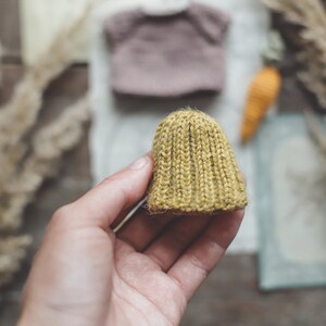Puede incluir: Un peque&ntilde;o gorro tejido a mano de color amarillo mostaza. El gorro est&aacute; hecho con un hilo grueso y tiene una textura acanalada.