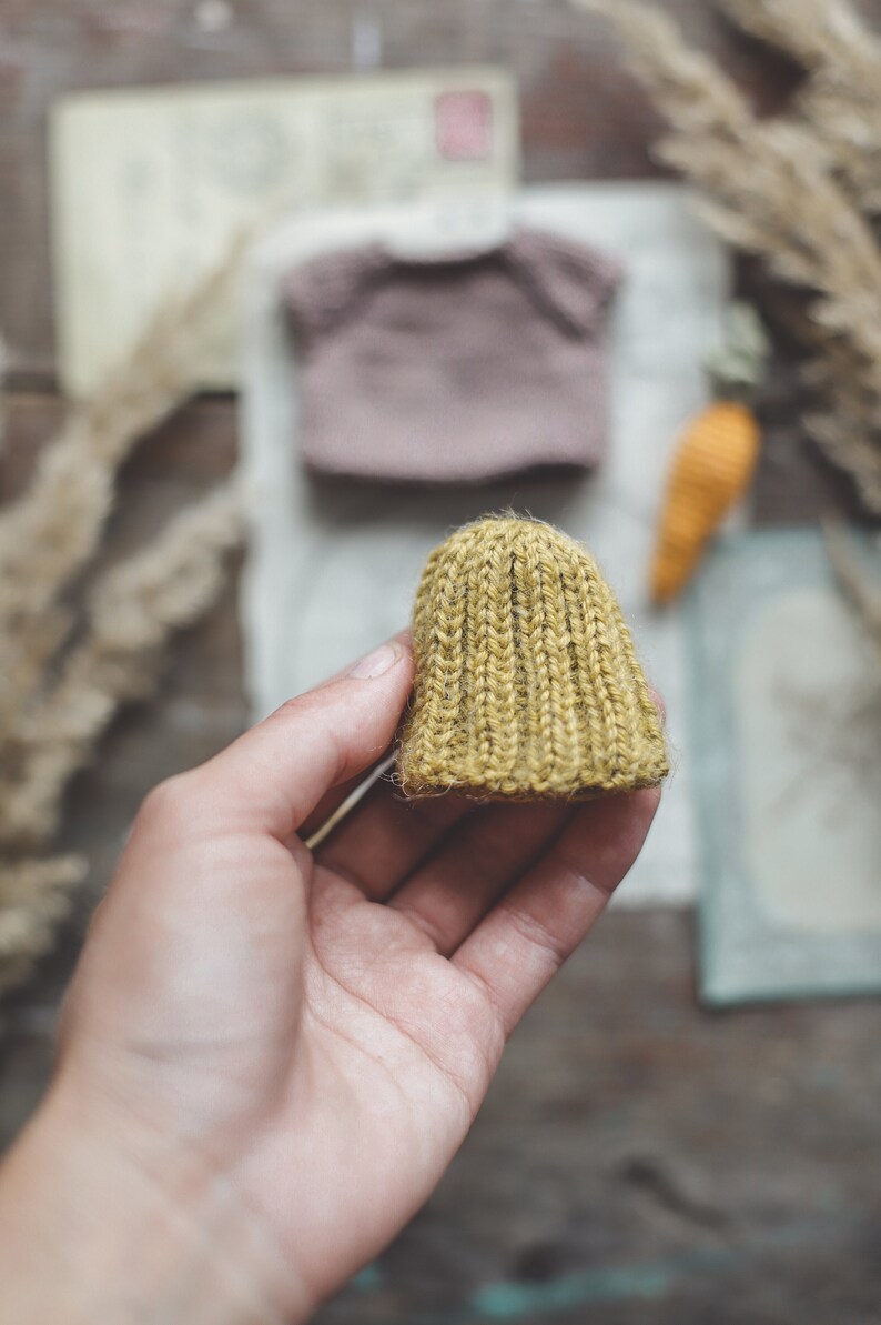 Puede incluir: Un peque&ntilde;o gorro tejido a mano de color amarillo mostaza. El gorro est&aacute; hecho con un hilo grueso y tiene una textura acanalada.