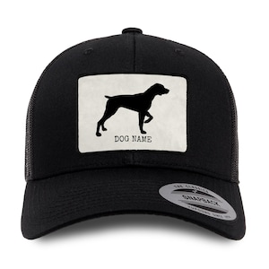 May include: Black trucker hat with a white patch featuring a silhouette of a dog breed. The patch has the text "DOG NAME" on it. The hat has a black mesh back and a black adjustable snap closure.
