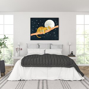 May include: A framed print of a tiger sleeping on a branch with a full moon and stars in the background. The print is hanging on a white wall above a bed with a gray knitted blanket.