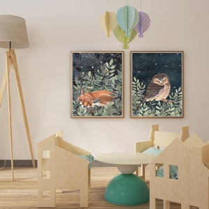 May include: Two framed illustrations of a fox and an owl sleeping in a forest setting with a starry night sky. The illustrations are hung on a white wall with a wooden floor and a wooden lamp.