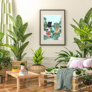 May include: A living room interior with a framed print of three tigers in a jungle setting. The print is hanging on a white wall above a wooden pallet couch with a green throw blanket. There are several potted plants in the room, including a large green plant in a brown pot, a smaller green plant in a wicker pot, and a small potted plant on a wooden coffee table.