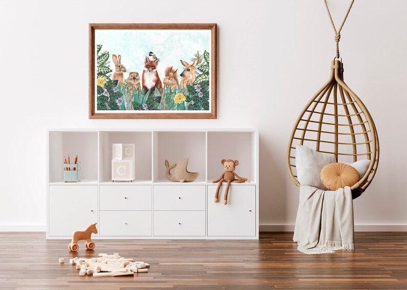 May include: A framed print of a whimsical woodland scene featuring a fox, rabbit, squirrel, deer, and a bird. The animals are surrounded by lush greenery and flowers. The print is in a light wood frame and is hanging on a white wall.