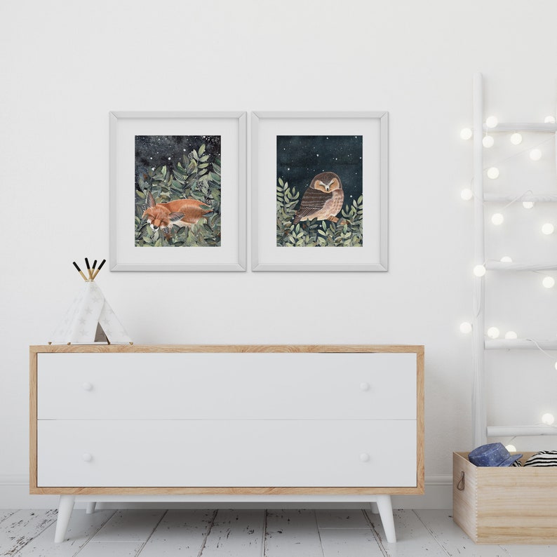 May include: Two framed illustrations of woodland animals against a dark blue background with white stars. The left illustration features a fox sleeping in a bed of green leaves. The right illustration features an owl perched on a branch with green leaves.