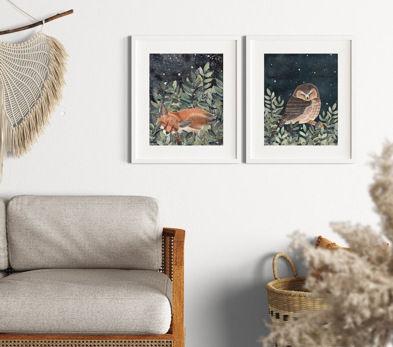 May include: Two framed illustrations of woodland animals. The first shows a fox sleeping in a bed of green leaves under a starry night sky. The second shows an owl perched on a branch with its wings folded, also under a starry night sky.
