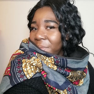 Puede incluir: Una mujer lleva una bufanda negra y azul con un patrón geométrico colorido. La bufanda está doblada y atada alrededor de su cuello.