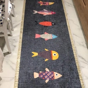 Puede incluir: Una alfombra de pasillo azul y blanca con un patrón repetitivo de peces coloridos. Los peces son de diferentes tamaños y tienen diferentes patrones. La alfombra tiene una textura tejida y un borde dorado.