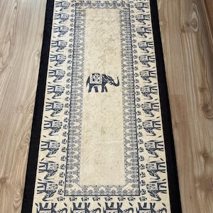 May include: A black and white rug with a border of elephants. The center of the rug is a cream color with a single elephant in the center.