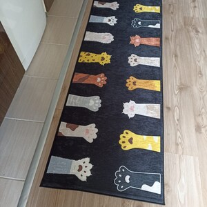 May include: A black and grey cat paw print rug with a variety of colored paw prints. The rug is rectangular and has a black border.