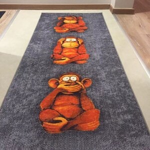 Può includere: Un tappeto grigio e arancione con tre scimmie che si coprono gli occhi, le orecchie e la bocca. Le scimmie sono sedute in fila sul tappeto.