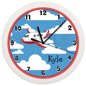 May include: A white and red airplane flies through a blue sky with white clouds. The clock face has black numbers and hands. The name "Kyle" is written below the airplane.