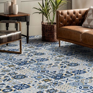 Puede incluir: Un azulejo de suelo estampado con un diseño azul, blanco y dorado. El azulejo está formado por varias formas geométricas y patrones florales. El azulejo se muestra en un salón con un sofá de cuero marrón y una mesa auxiliar de madera.