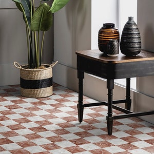 Puede incluir: Una mesa auxiliar negra con una tapa de madera y patas torneadas se encuentra sobre un suelo de baldosas rojas y blancas. Tres jarrones decorativos, uno marrón y rayado, uno negro y rayado y uno blanco con una superficie texturizada, están sobre la mesa.