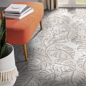 May include: A light grey area rug with a brown line drawing of tropical leaves. An orange bench with three books stacked on top sits on the rug.