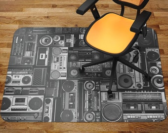 May include: A black and white patterned floor mat featuring a repeating design of vintage boomboxes and cassette players. The mat is placed on a wooden floor and a yellow office chair is sitting on top of it.