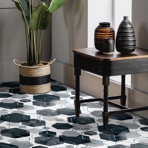 Op de afbeelding: Een zwarte bijzettafel met een houten blad staat op een geometrisch betegelde vloer. Drie decoratieve vazen, een bruine, een zwart-wit en een grijze, zijn op de tafel gerangschikt.