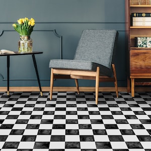 Puede incluir: Un suelo de ajedrez negro y blanco con un sillón gris y una mesa auxiliar negra con un jarrón de flores amarillas.