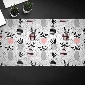 May include: A white desk mat with a repeating pattern of black and pink potted plants. The plants are in various shapes and sizes, and the pattern is set against a white background with small black dots.