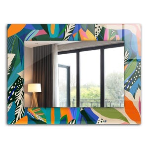 Puede incluir: Espejo de pared rectangular con un borde de patrón floral vibrante y colorido. El diseño presenta una mezcla de hojas y formas abstractas naranjas, azules, verdes y rosas. El espejo refleja una habitación con ventana, cortinas y lámpara.