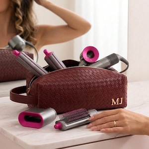 May include: A dark red woven leather toiletry bag with the gold initials MJ embossed on the front. The bag contains a grey and fuchsia hair styling tool with multiple attachments, including a brush, a nozzle, and two cylindrical curling barrels.