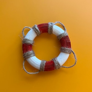 May include: A small white and red life preserver with brown rope accents.