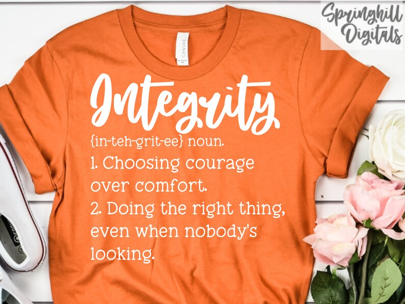 May include: Orange t-shirt with white text that reads "Integrity {in-teh-grit-ee} noun. 1. Choosing courage over comfort. 2. Doing the right thing, even when nobody's looking."