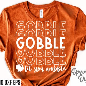 May include: Orange t-shirt with white text that reads "Gobble til you wobble" with a turkey graphic. The text is repeated in a layered, stacked design.