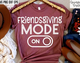 May include: A maroon t-shirt with the text "Friendsgiving Mode On" in white with a white circle around the word "On" and a white circle with a line through it to the left of the word "On".