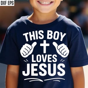 Op de afbeelding: Een marineblauw T-shirt met de tekst "THIS BOY LOVES JESUS" in het wit. Het ontwerp bevat een kruis en duim omhoog symbolen. Het T-shirt wordt door een kind gedragen.
