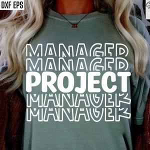 Könnte beinhalten: Salbeigrünes T-Shirt mit den weißen Worten "MANAGED PROJECT MANAGER", vertikal gestapelt. Das Design hat einen geschichteten Effekt, wobei jedes Wort leicht versetzt ist. Das Shirt wird von einer Person mit blonden Haaren getragen.