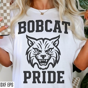 May include: White t-shirt with a black graphic of a bobcat head and the words "BOBCAT PRIDE". The design is centered on the shirt. The image also includes the text "SVG PNG DXF EPS".