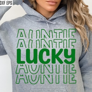 Puede incluir: Una sudadera con capucha gris con un gráfico verde que dice "Auntie Lucky" en una fuente apilada y con contorno.